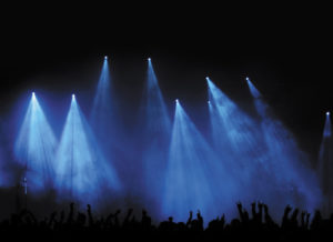 Konzert- oder Festivalpublikum als Silhouette vor blauem Licht - Hunderte von Fans feiern mit erhobenen Haenden eine Band