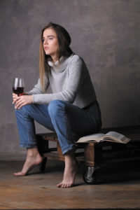 Model in sweater and jeans holding wineglass, girl with wineglass, high fashion look, sitting girl, beautiful girl, blonde girl, isolated, model in studio, girl wearing jeans and sweater, long hair, gray background